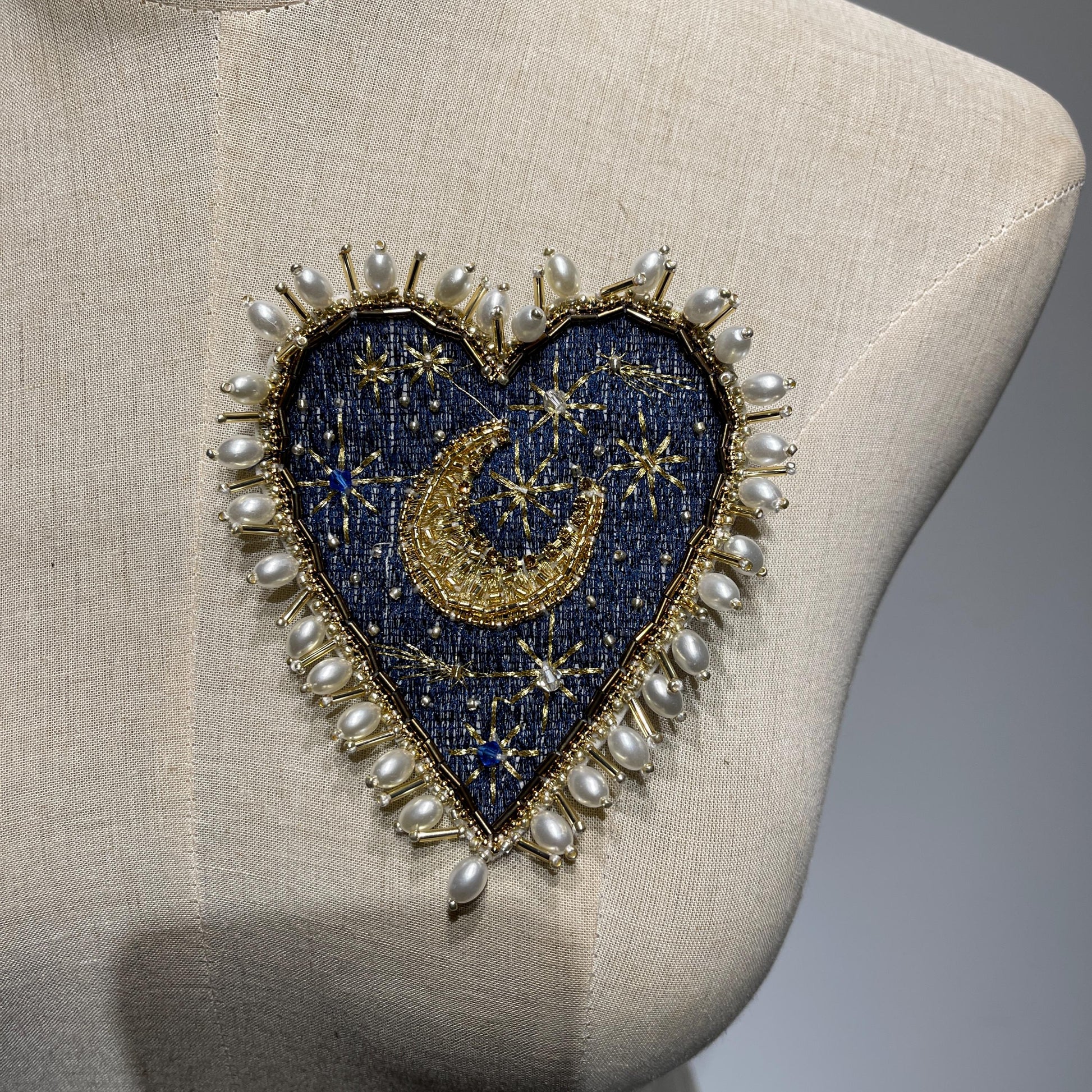Front hero view of the 11.5x10cm Hand-Beaded Celestial Moon patch with a navy denim base, displayed beautifully on a beige linen dress form mannequin, showcasing the luxury outer border of irregular baroque pearls and gold thread constellations.