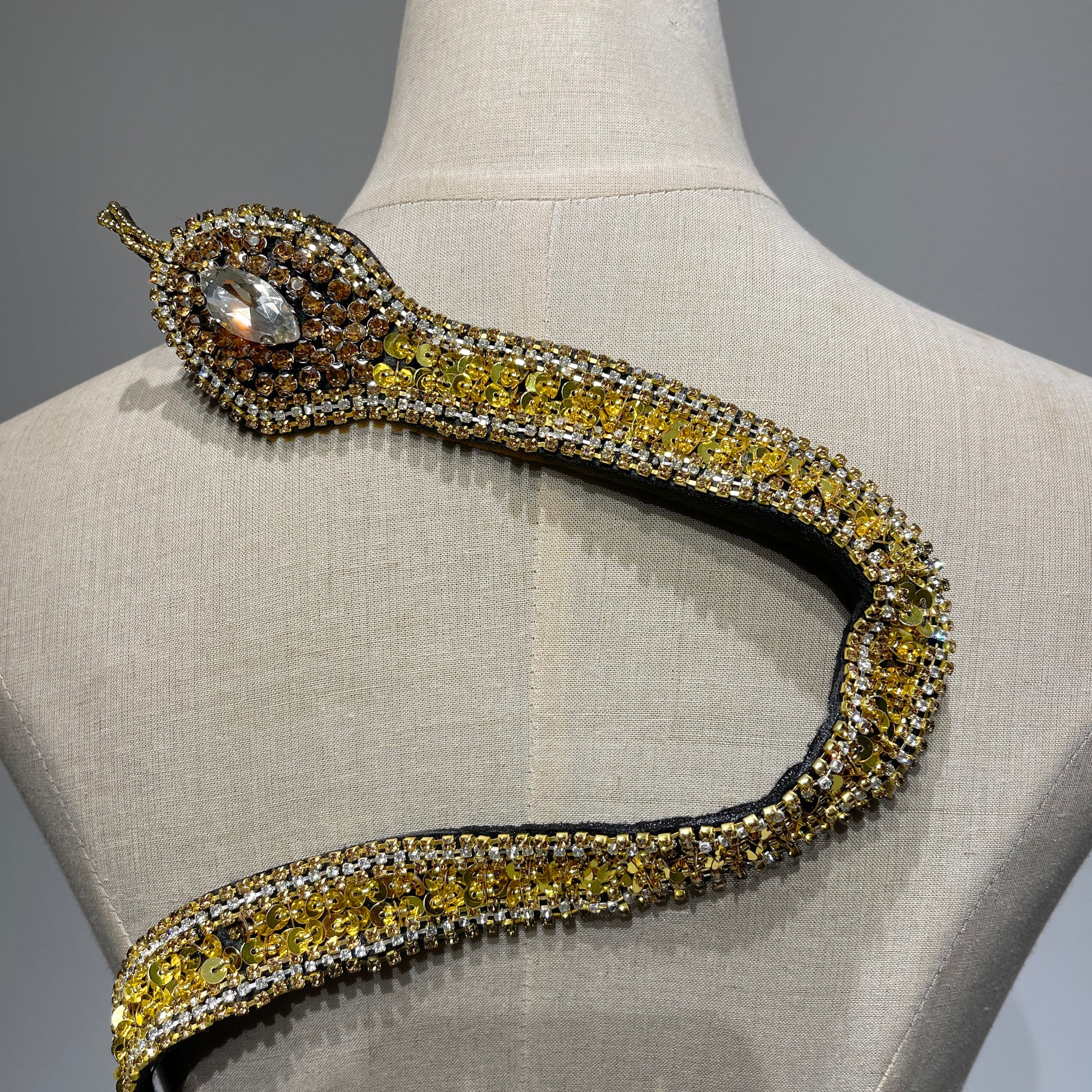 Close-up detail of a handcrafted gold snake patch head, featuring a large crystal eye, premium gold rhinestones, and meticulously hand-stitched sequins.