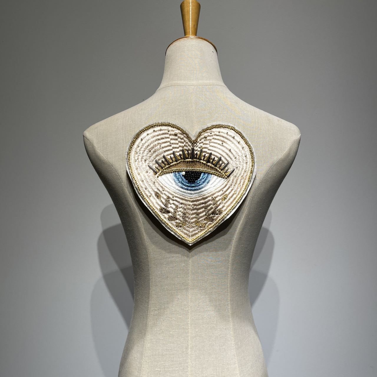 Luxurious 19cm hand-beaded sacred heart evil eye embroidery patch displayed on a clothing mannequin backpiece, showcasing 3D crystal bugle beads and metallic gold couture details for custom jacket DIY.