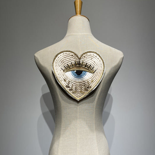 Luxurious 19cm hand-beaded sacred heart evil eye embroidery patch displayed on a clothing mannequin backpiece, showcasing 3D crystal bugle beads and metallic gold couture details for custom jacket DIY.