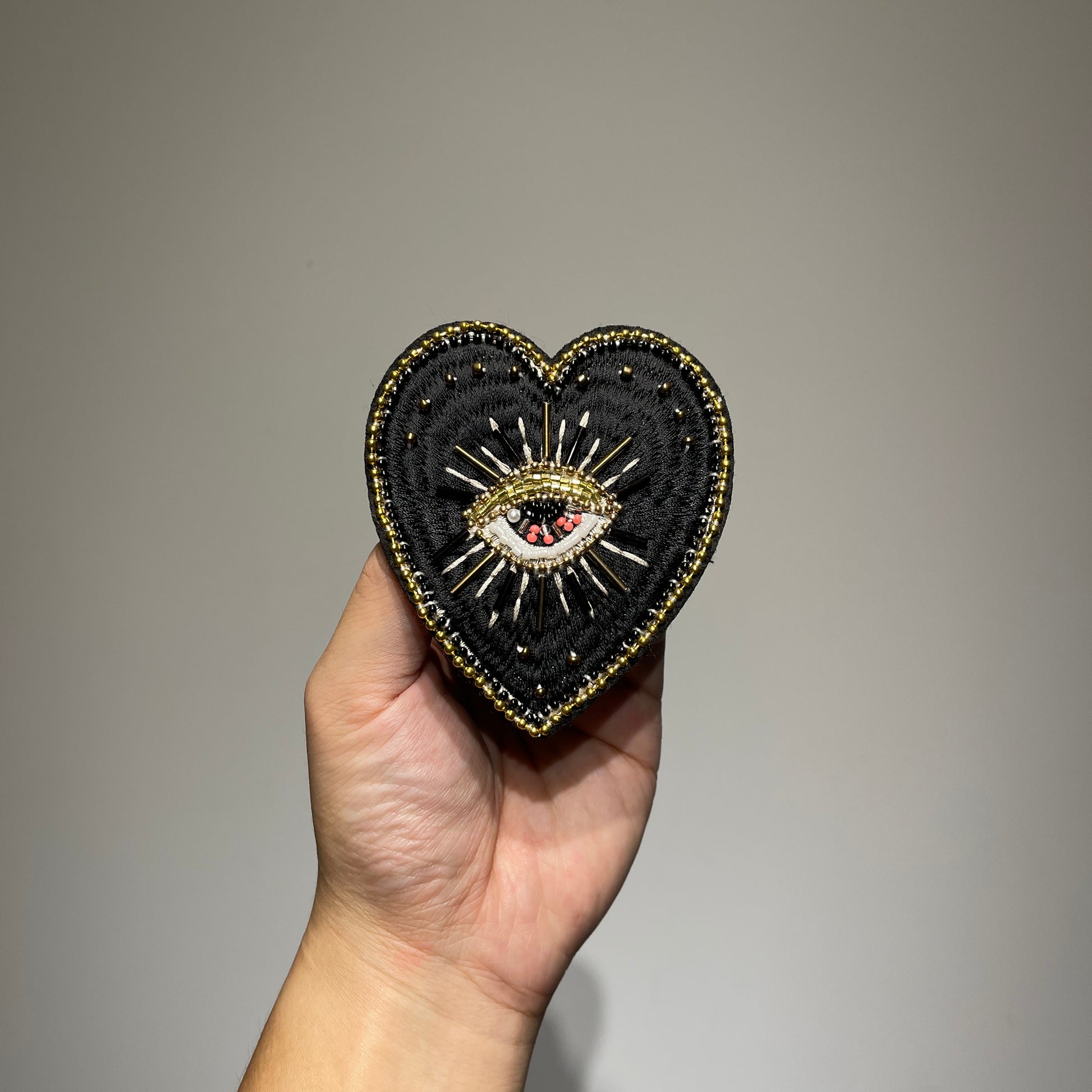 Handmade black evil eye beaded heart patch featuring gothic gold embroidery, faux pearls, and seed beads for DIY fashion - 9x8.5cm.⁠