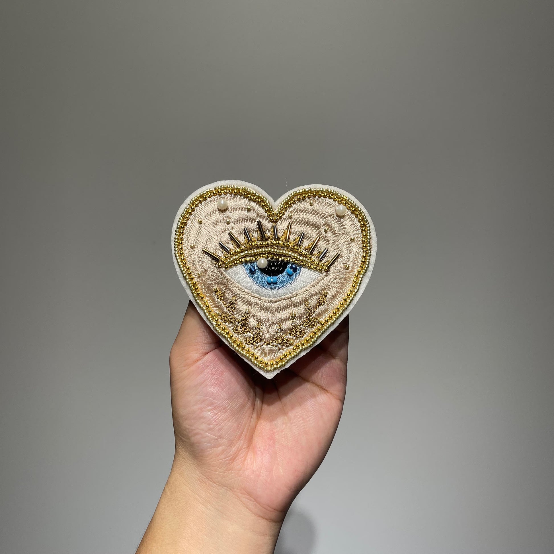 ⁠Handmade 10cm evil eye beaded heart patch featuring gold metallic embroidery, faux pearls, and glass seed beads for DIY fashion and jacket repair.⁠
