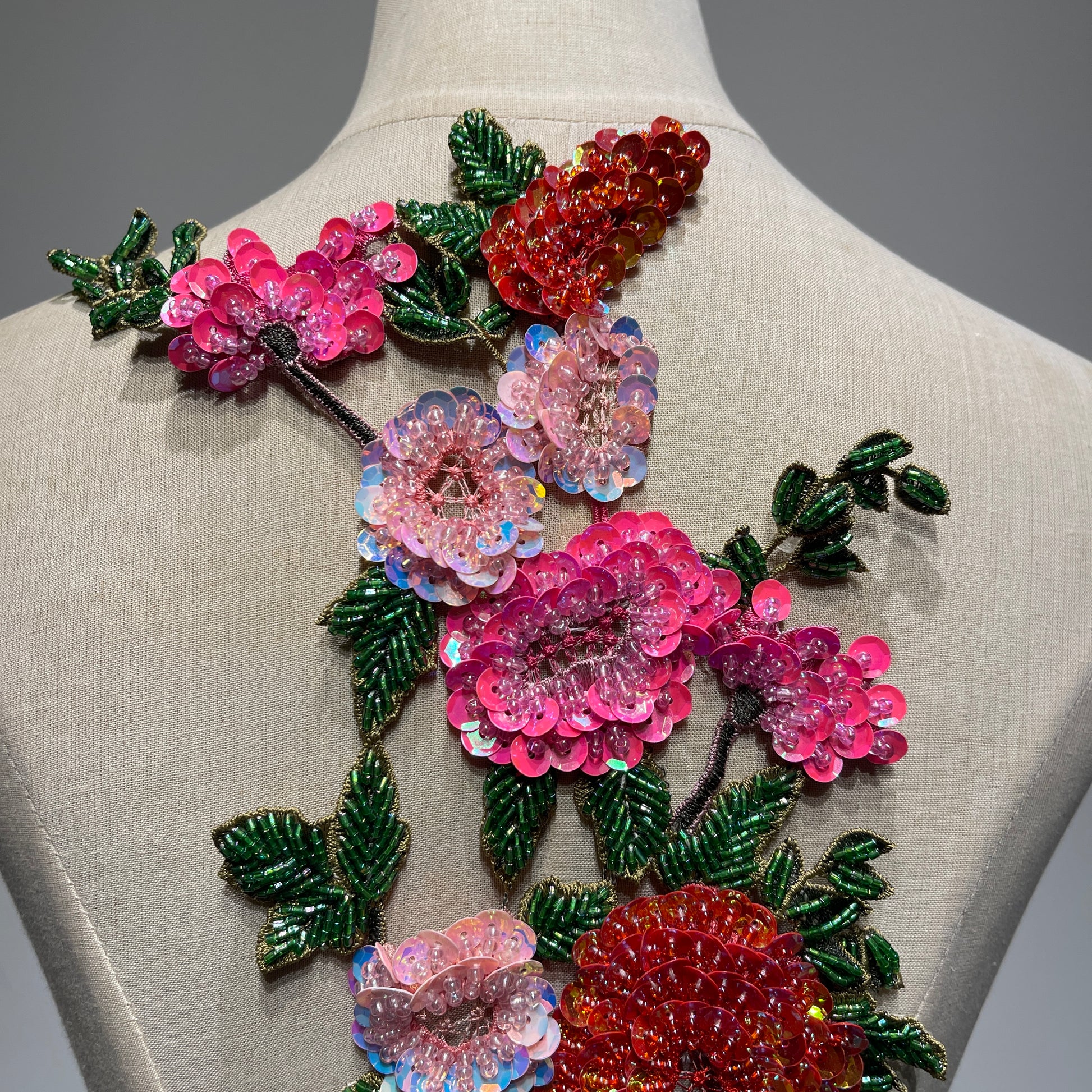 An ultra-close-up of the haute couture embroidery and beadwork, showing high-luster pink sequins, glass bugle beads on green leaves, and premium craftsmanship textures.⁠