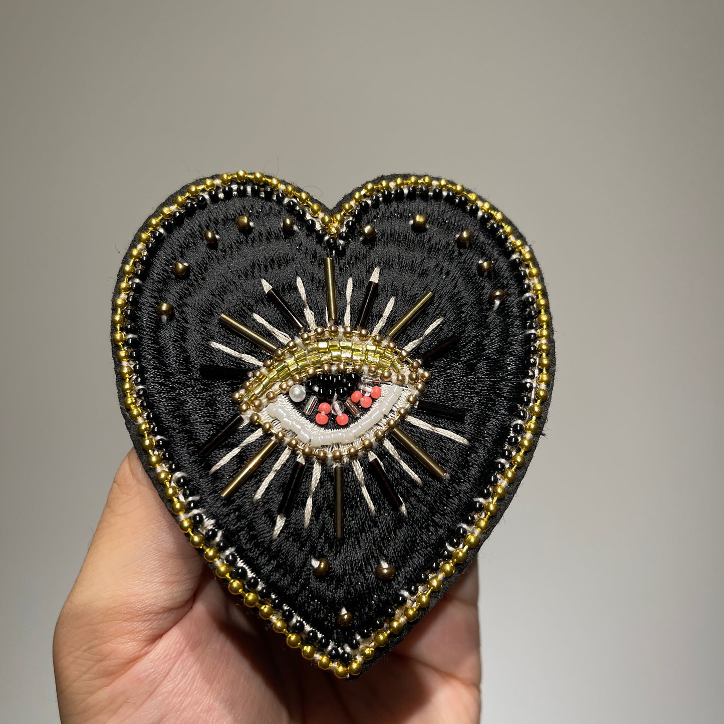 ⁠Close-up view of artisanal hand-stitched black and gold embroidery with pearl and beadwork on an evil eye heart patch - 9x8.5cm.⁠