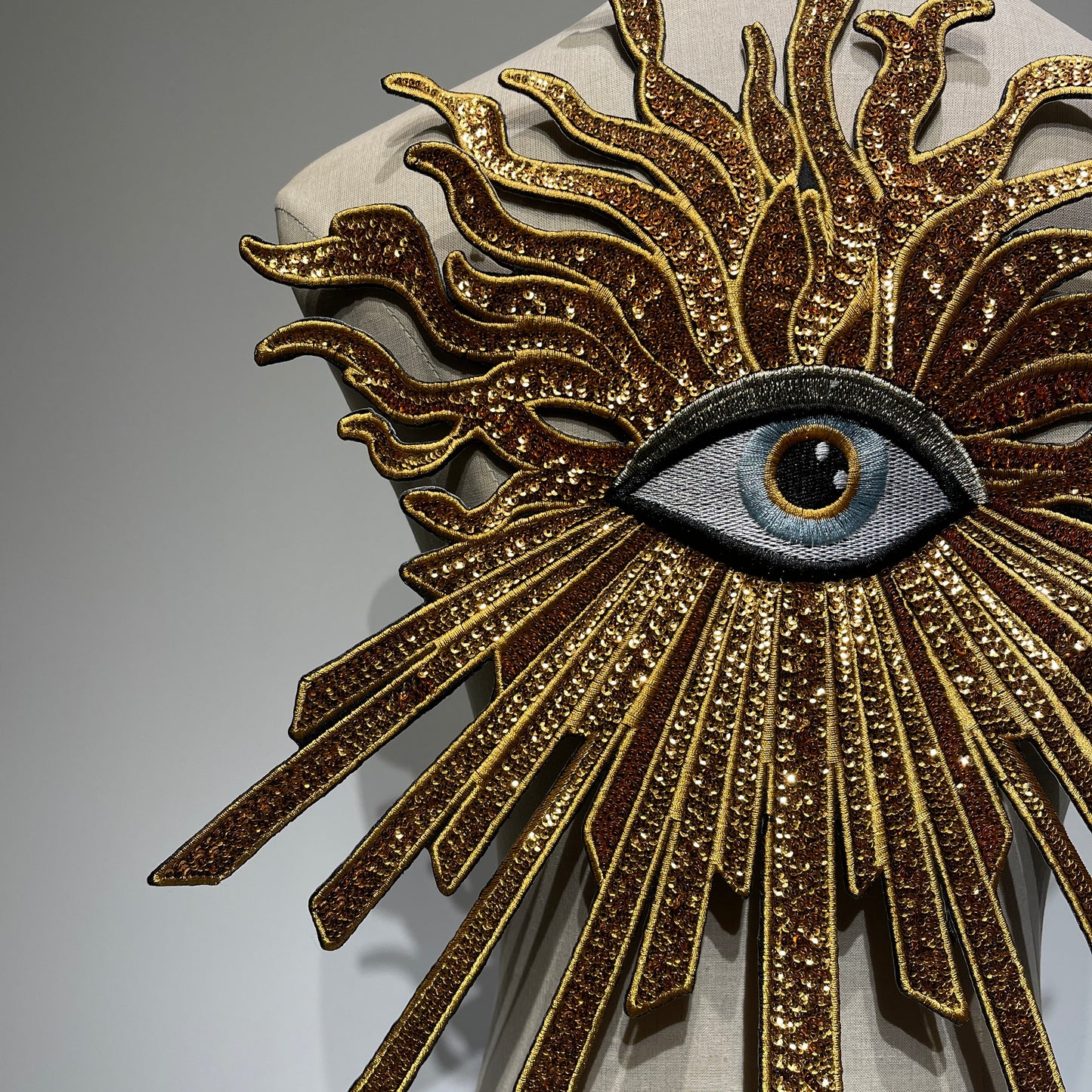Close-up detail of handcrafted luxury golden evil eye patch, showcasing glittering gold sequins, premium shimmering threads, and heavy-industry embroidery needlework.