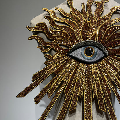 Close-up detail of handcrafted luxury golden evil eye patch, showcasing glittering gold sequins, premium shimmering threads, and heavy-industry embroidery needlework.