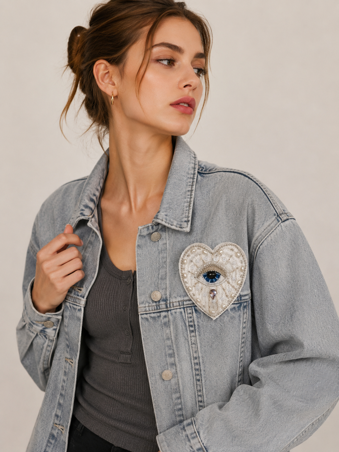 Model wearing a light blue denim jacket styled with a handmade white evil eye beaded heart patch - 9.5x8cm.
