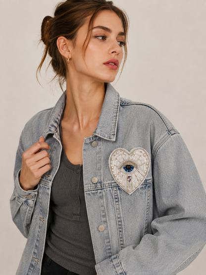 Model wearing a light blue denim jacket styled with a handmade white evil eye beaded heart patch - 9.5x8cm.