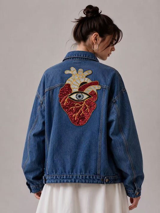 Back view of a female model wearing a blue denim jacket with the oversized anatomical heart and evil eye sequin patch.⁠