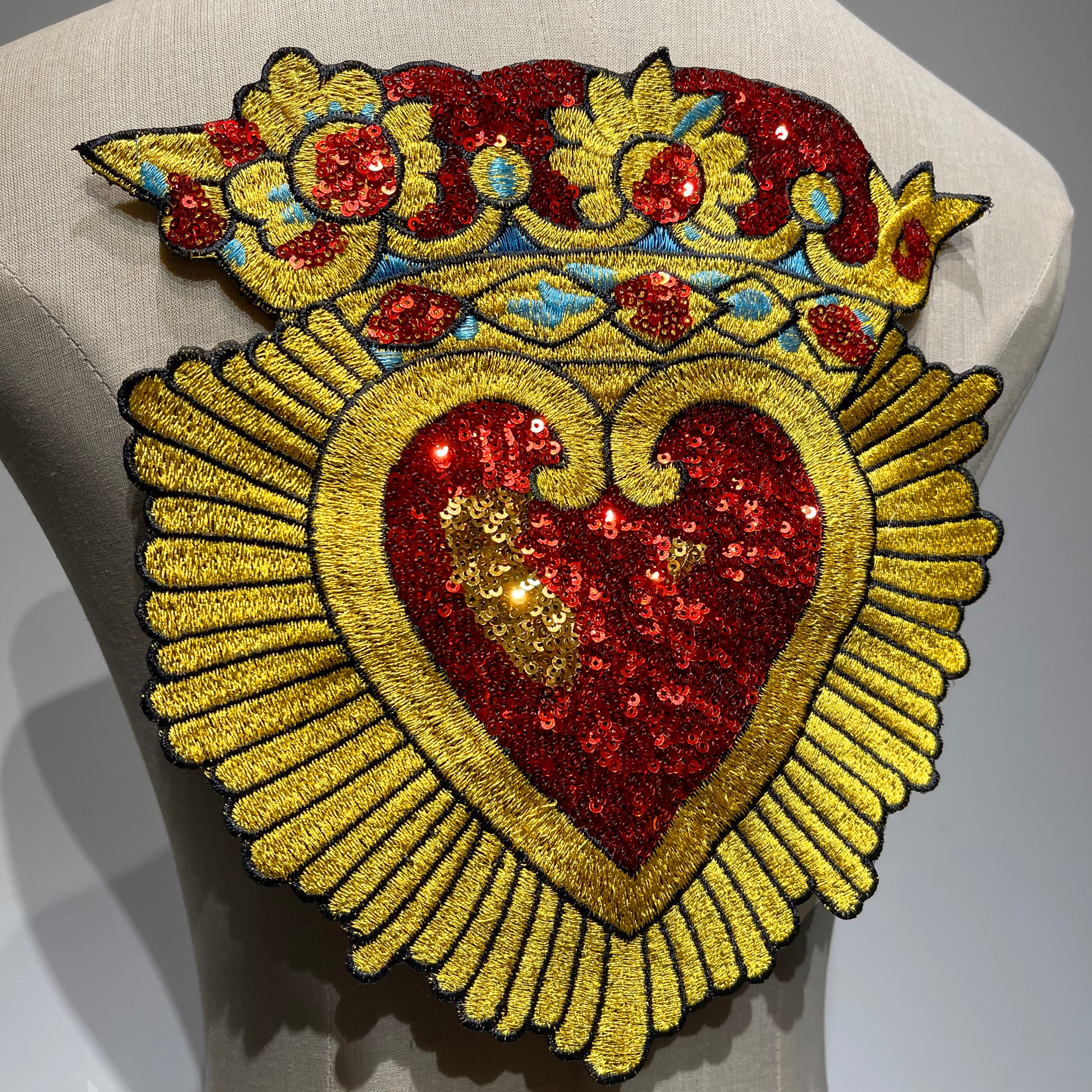 Front view of the large Sacred Heart crown patch, catching the light to highlight the sparkling red and gold sequins and detailed embroidery border.