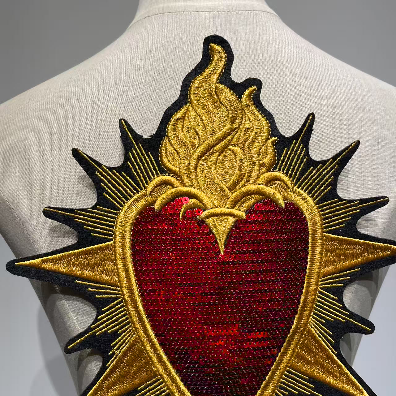 Close up detailed view of the Sacred Heart embroidered jacket patch showcasing heavy red sequins and intricate gold metallic stitching on a garment mannequin
