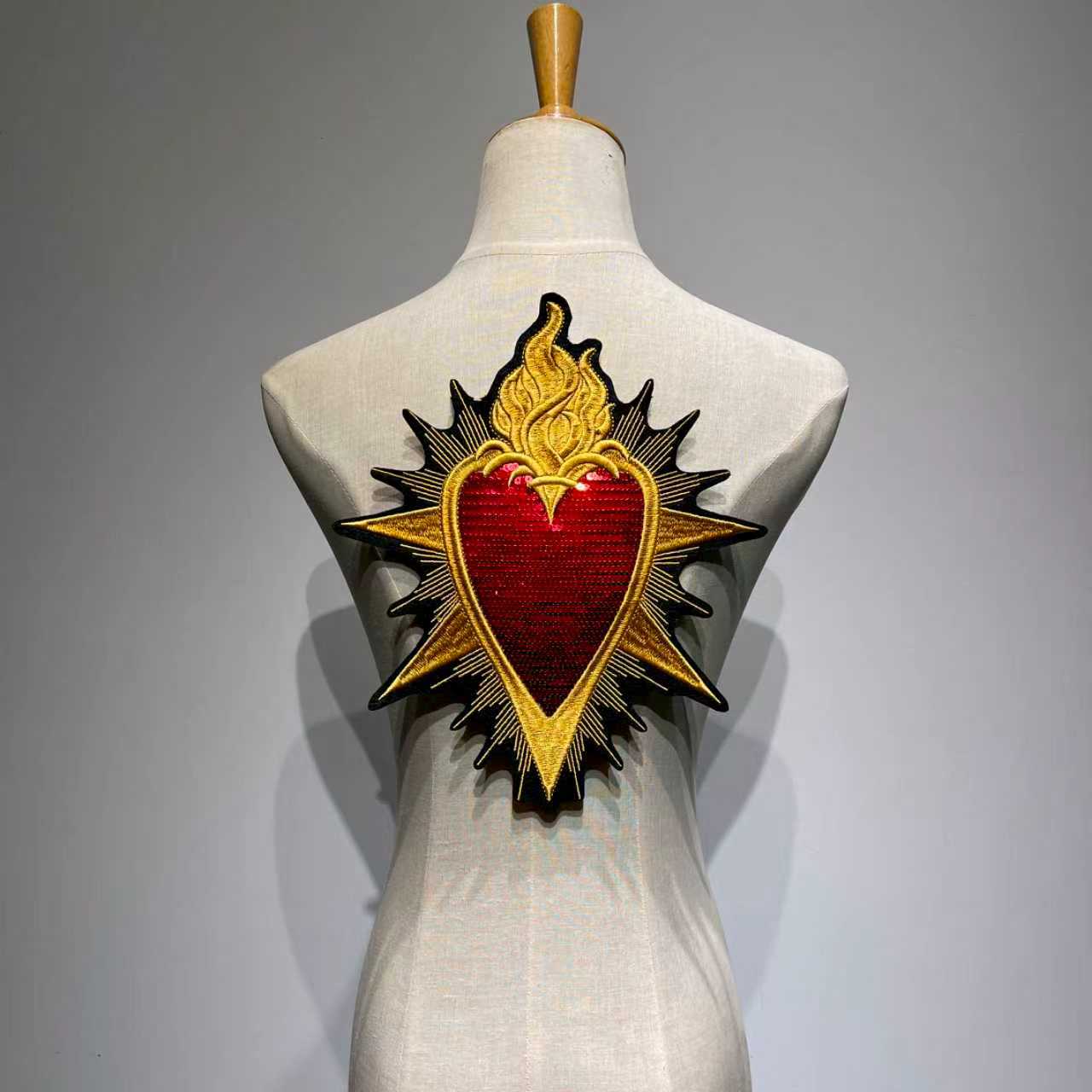 Oversized Sacred Heart embroidered jacket patch with shimmering red sequins and metallic gold baroque flames on a clothing mannequin back view