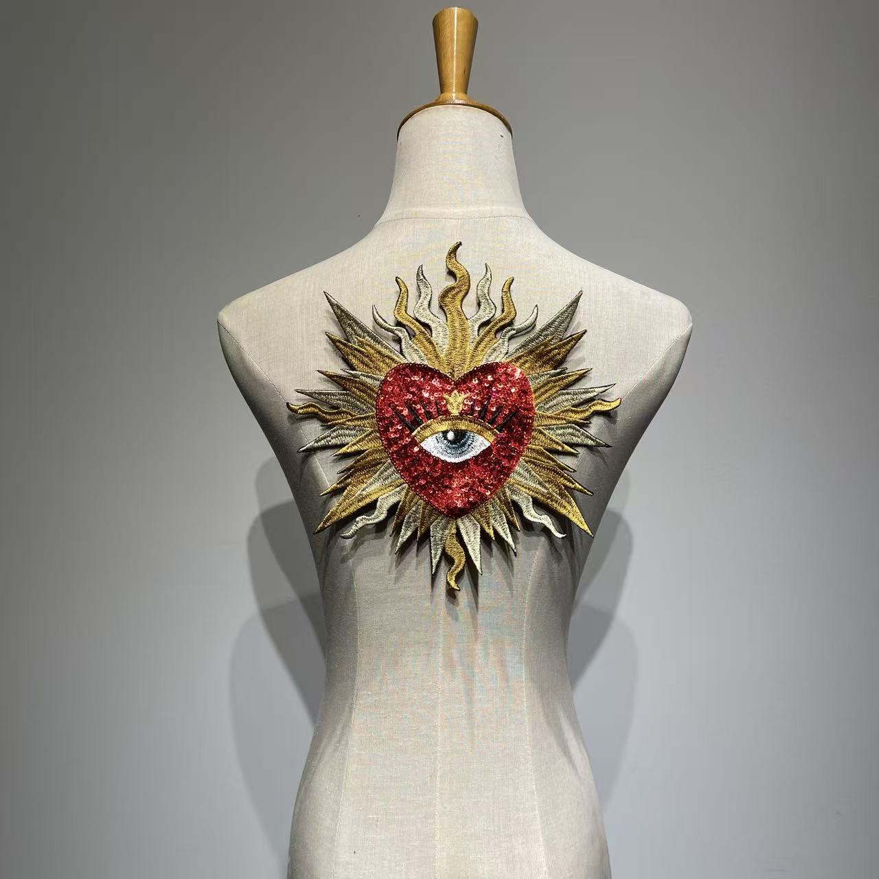 Luxury red sacred heart sequin patch on a mannequin, handcrafted medium-large flaming sunburst and evil eye embroidery patch for jacket DIY custom fashion.
