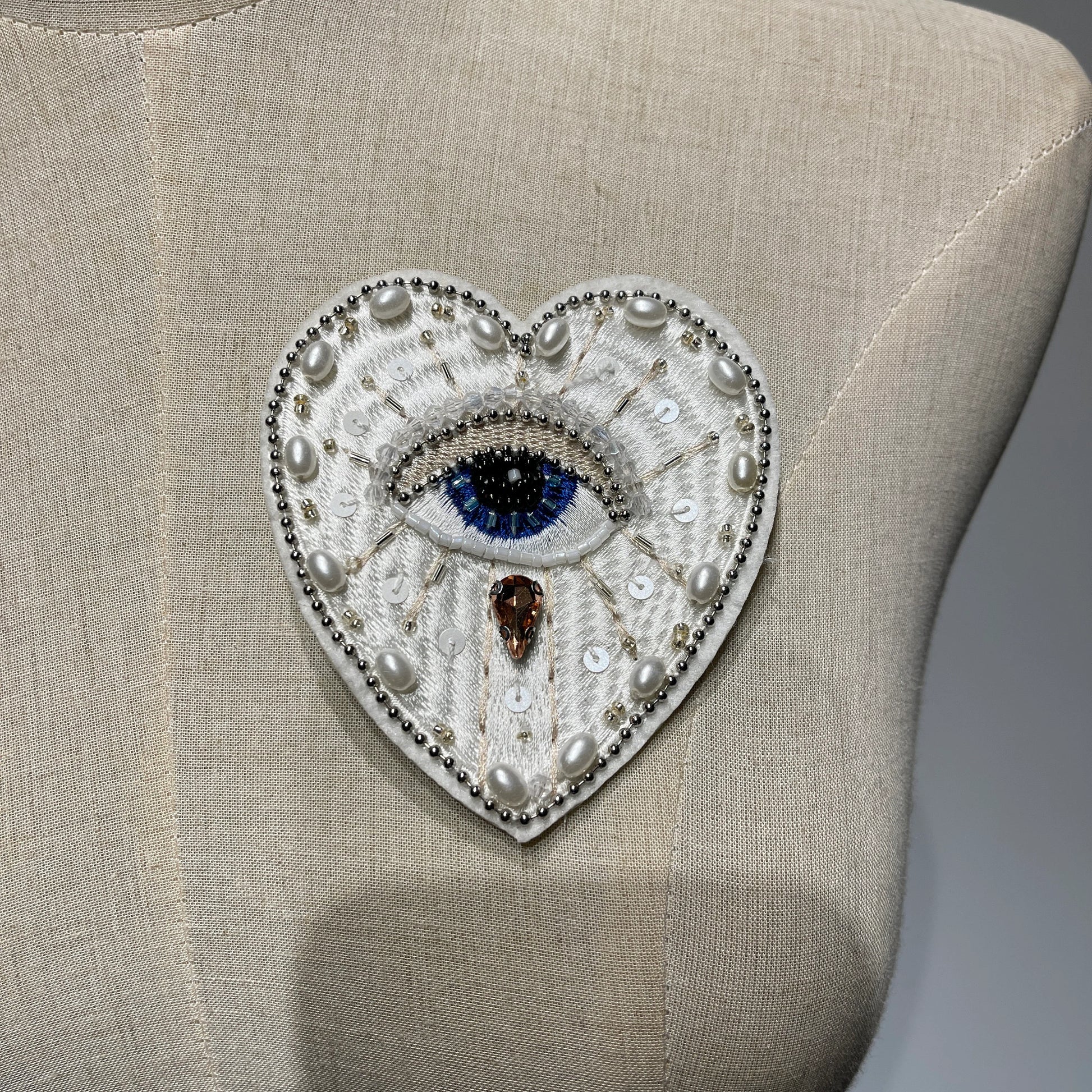 Mannequin display showcasing a handmade white evil eye beaded heart patch with pearls and sequins - 9.5x8cm.